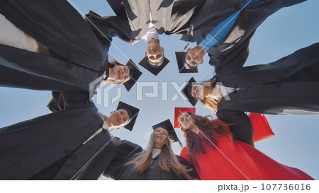 College graduates in a circle stand hugging each other. 107736016