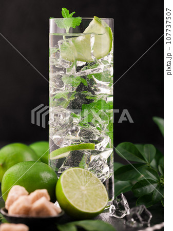 Highball glass of Mojito cocktail with ice cubes,mint and lime on black board with fresh limes 107737507