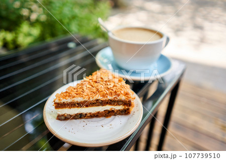 Cup of hot Peanut latte and Carrot pie. The table in the coworking space of the coffee shop. A cup of coffee on the veranda on a sunny day. Coffee break at the cafe. Close-up 107739510