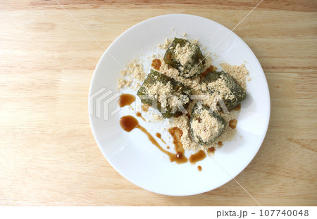 Matcha Warabi Mochi with Kinako powder and brown sugar syrup in white plate on wooden table, traditional Japanese dessert 107740048