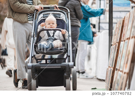 Mother walking and pushing his infant baby boy child in stroller in crowd of people wisiting sunday flea market in Malaga, Spain 107740782
