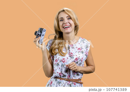 Happy blonde cheerful woman with retro photo camera. Isolated on beige. 107741389