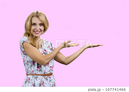 Happy caucasian woman shows copy space with both hands. Isolated on pink. Happy caucasian woman shows copy space with both hands. Isolated on pink. 107741466