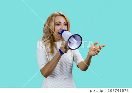Attractive expressive blonde woman screaming in megaphone. Isolated on turquoise. 107741678