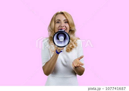 Happy positive blonde woman giving a speech in megaphone. Isolated on pink. 107741687
