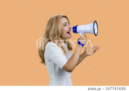 Attractive mature blonde woman screaming in megaphone. Isolated on beige. 107741688
