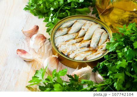 Canned small sardines in oil on background with greens Canned small sardines in oil on background with greens 107742104
