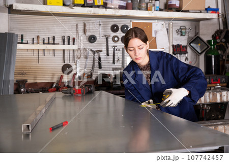 Woman working with metal sheet and using measuring tape 107742457