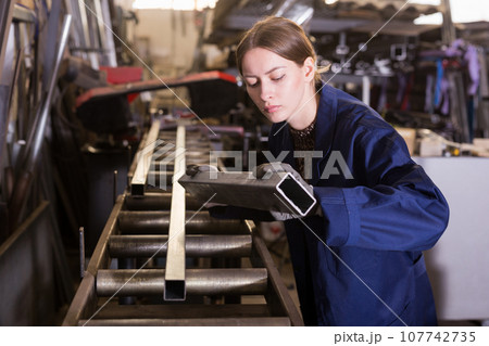 Female worker cuts metal profile pipe on a band saw 107742735