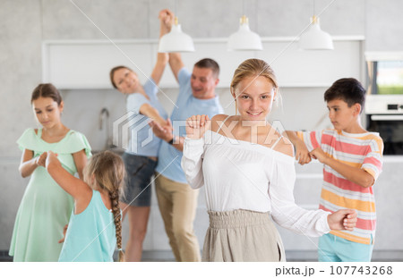 Behind cheerful girl, big family of parents, sisters, brother is rejoicing, dancing, having fun. 107743268