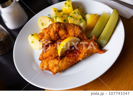 Chicken fillet in batter with Parmesan with potatoes and pickled cucumbers Chicken fillet in batter with Parmesan with potatoes and pickled cucumbers 107743347