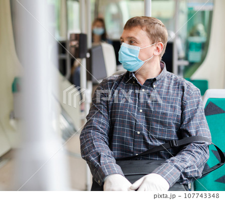 Man in medical mask riding city bus 107743348