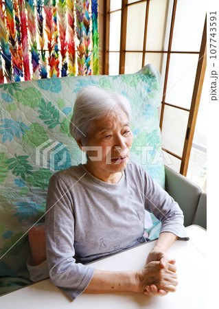 リクライニングした介護ベッドに座って正面を見つめる白髪のシニア女性 107743591