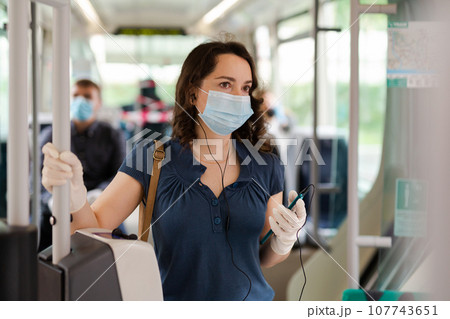 Modern girl in protective medical mask and gloves traveling in tram and using mobile phone 107743651