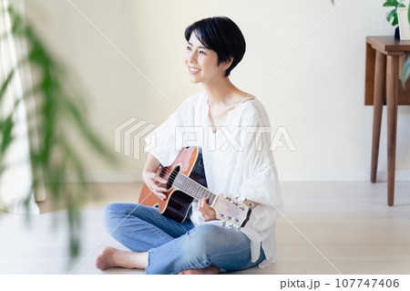 部屋でギターを抱える女性 107747406