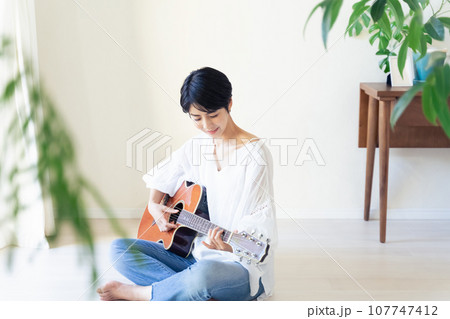 部屋でギターを抱える女性 107747412