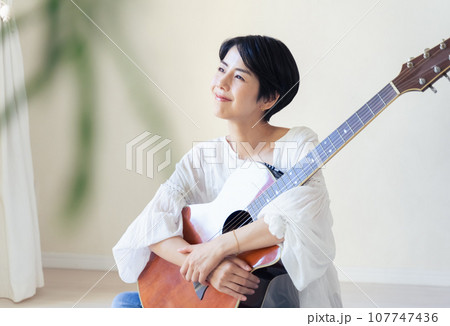 部屋でギターを抱える女性 107747436