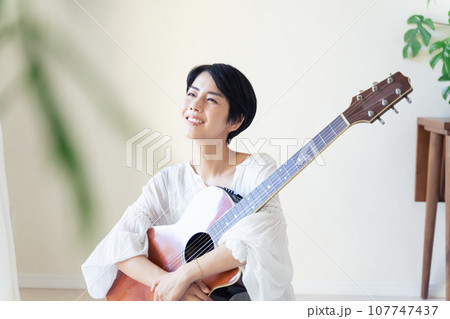 部屋でギターを抱える女性 107747437