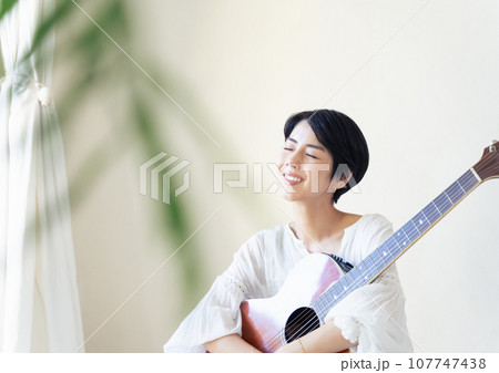 部屋でギターを抱える女性 107747438