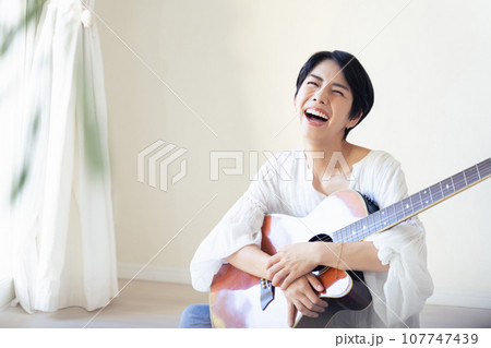 部屋でギターを抱える女性 107747439