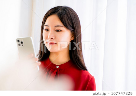 窓際でスマホを見る女性 107747829