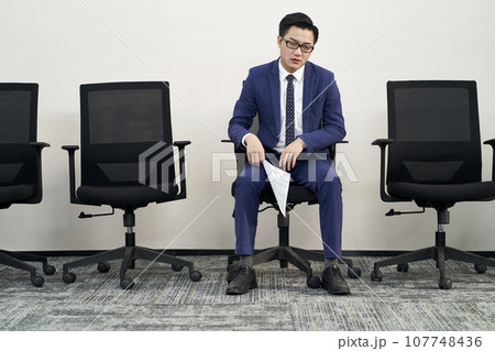 young male asian job seeker sitting in chair appears to be frustrated and defeated young male asian job seeker sitting in chair appears to be frustrated and defeated 107748436