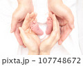 赤ちゃんの小さな足を包むママとパパの手 107748672