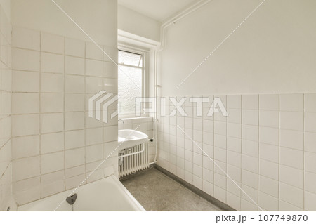 a bathroom with white tiles on the walls and floor, along with a bathtub in the corner of the room 107749870