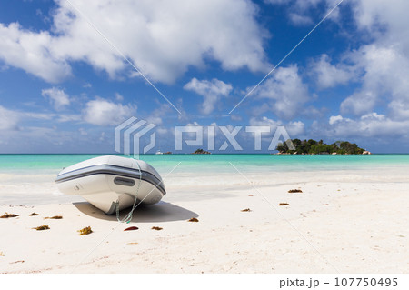An inflatable motor boat lays on white sand on a sunny day. Seychelles beach An inflatable motor boat lays on white sand on a sunny day. Seychelles beach 107750495