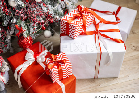 A variety of colored Christmas gifts stand near a decorative Christmas tree in the house on the floor under the branches. 107750836