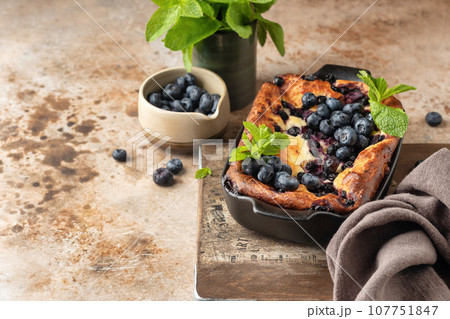 Cottage cheese casserole with blueberries and mint leaves deciration in baking dish on brown textured background with text space 107751847