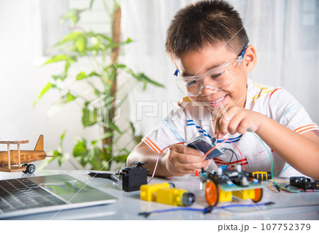 Asian kid boy plugging energy and signal cable to sensor chip with Arduino robot car, Little child remotely learn online with car toy, STEAM education AI technology course school learning lesson 107752379