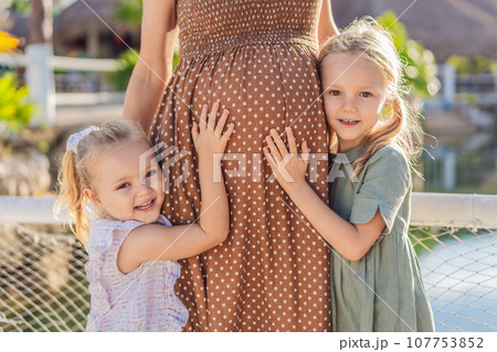 Sisters' love blooms as they tenderly embrace their mother's pregnant belly, sharing anticipation and affection for their soon-to-arrive sibling Sisters' love blooms as they tenderly embrace their mother's pregnant belly, sharing anticipation and affection for their soon-to-arrive sibling 107753852