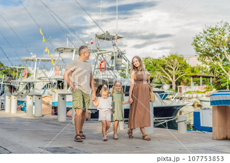 A happy, mature couple over 40 with their two daughters enjoying a leisurely walk on the waterfront, their joy evident as they embrace the journey of pregnancy later in life A happy, mature couple over 40 with their two daughters enjoying a leisurely walk on the waterfront, their joy evident as they embrace the journey of pregnancy later in life 107753853
