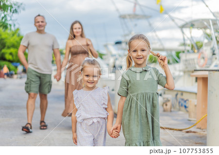 A happy, mature couple over 40 with their two daughters enjoying a leisurely walk on the waterfront, their joy evident as they embrace the journey of pregnancy later in life 107753855