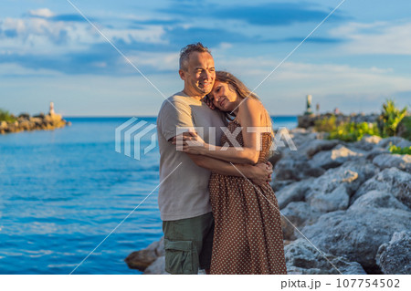 A happy, mature couple over 40, enjoying a leisurely walk on the waterfront On the Sunset, their joy evident as they embrace the journey of pregnancy later in life A happy, mature couple over 40, enjoying a leisurely walk on the waterfront On the Sunset, their joy evident as they embrace the journey of pregnancy later in life 107754502