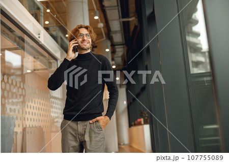 Smiling male sales manager is talking phone standing in modern coworking and looks away Smiling male sales manager is talking phone standing in modern coworking and looks away 107755089
