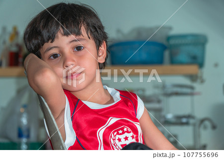 A boy wear red shirt sitting in the kitchen during waiting for a meal 107755696