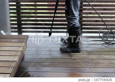 高圧洗浄機でウッドデッキの汚れを綺麗にしている様子　長靴を履いた男性が作業 107756926