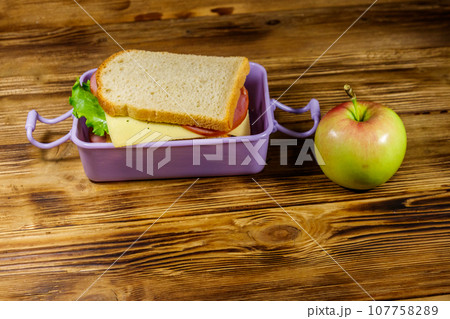 Lunch box with sandwiches and apple on a wooden table Lunch box with sandwiches and apple on a wooden table 107758289