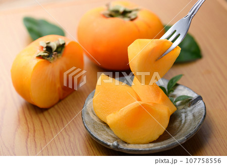 とっても甘い秋の味覚 皿に盛り付けた 柿をフォークでつまむ フルーツ （テーブルバック）柿の実 かき 107758556