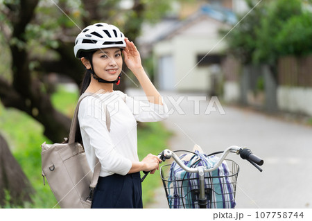 ヘルメットに手を添えて、自転車の横に立つ若い女性 107758744