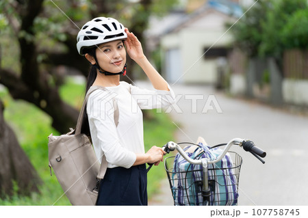 ヘルメットに手を添えて、自転車の横に立つ若い女性 107758745