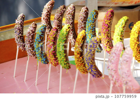 縁日の露店に並んだチョコバナナの写真。色とりどりに並べられて美味しさを競うように手に取られるのを待つ 縁日の露店に並んだチョコバナナの写真。色とりどりに並べられて美味しさを競うように手に取られるのを待つ 107759959