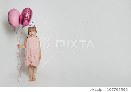 Cheerful child holding two pink balloon on white studio wall banner background.  107765596