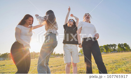 Funny jolly friends dancing in the city meadow in the evening. Funny jolly friends dancing in the city meadow in the evening. 107765917