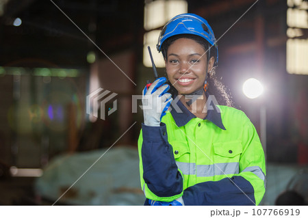 Industrial robotics engineer female american african holding walkie talkie looking at camera. Industrial robotics engineer female american african holding walkie talkie looking at camera. 107766919