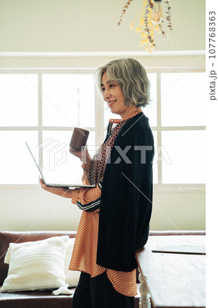 ドリンクを手にパソコンを操作するシニア女性 ドリンクを手にパソコンを操作するシニア女性 107768363