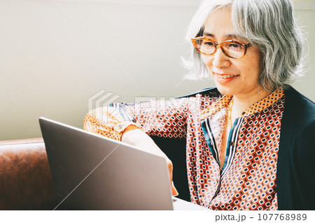 ソファでくつろぎながらPCを見つめるシニア女性 107768989
