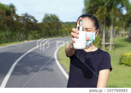 Young woman in medical protective mask and holding an alcohol in hand. campaign to use protective mask and alcohol  for protect COVID19 107769993